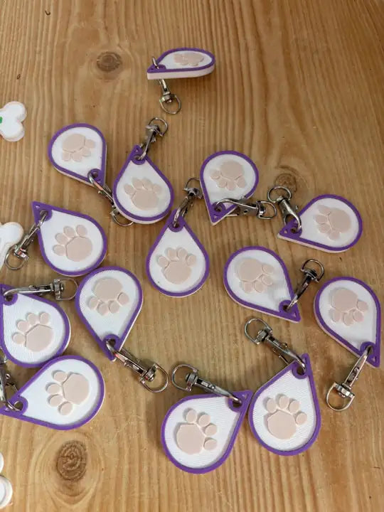 A batch of Raindrop Paw Keyrings printed in purple, white and peach, with silver clips